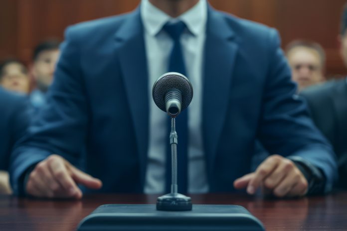 Microphone on a wooden table with a speaker in a suit in the background